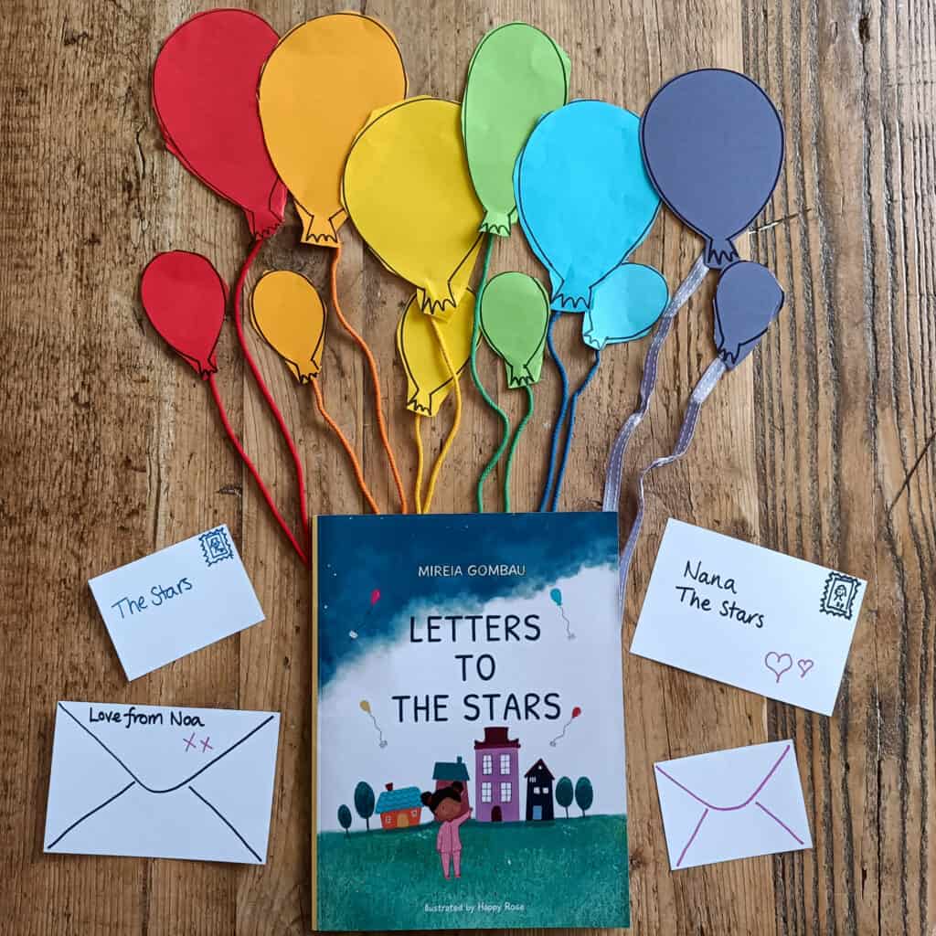 Letters to the Stars Book lay on a table with paper balloons and thread coming from balloons in a rainbow of colours. Little letters to the sides.