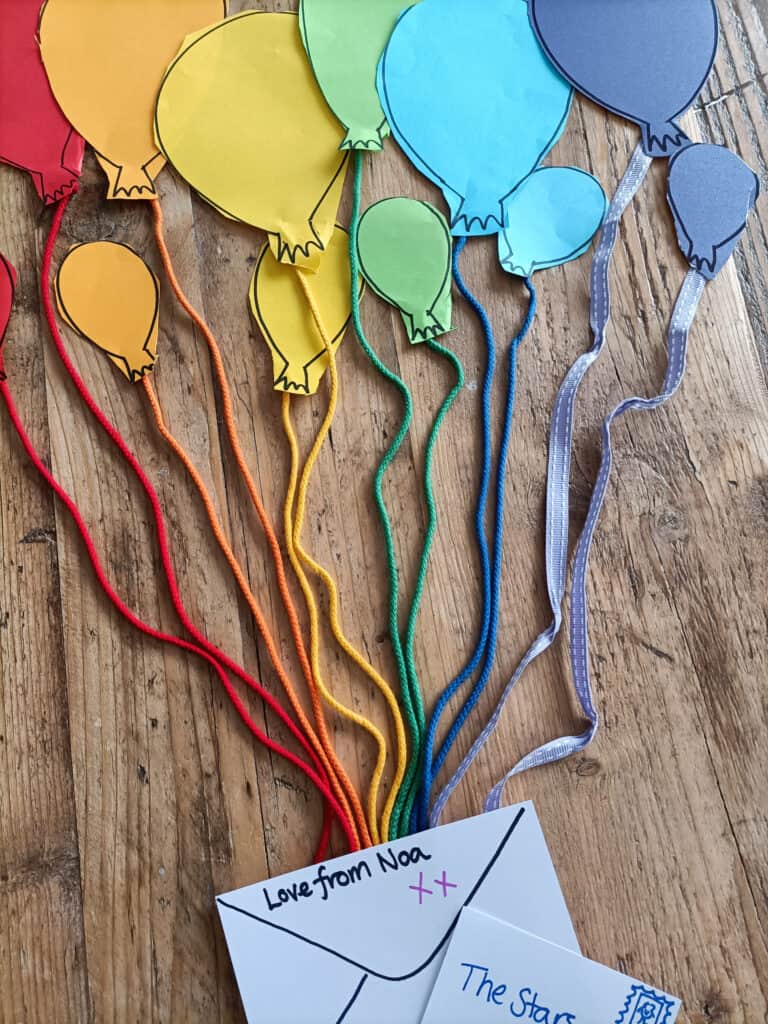 Paper balloons and thread coming from balloons in a rainbow of colours. Little letters to the sides.