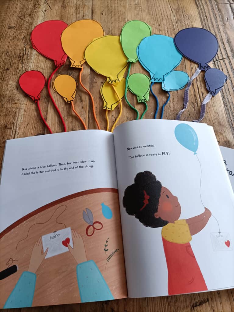 Letters to the Stars Book lay on a table (open page)with paper balloons and thread coming from balloons in a rainbow of colours. Little letters to the sides.