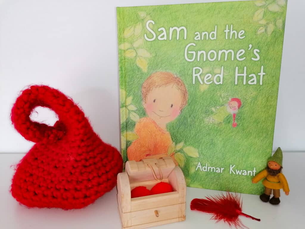 Sam and the Gnome's Red Hat book stands with a red crochet hat to the left and treasure chest with red feather in the foreground