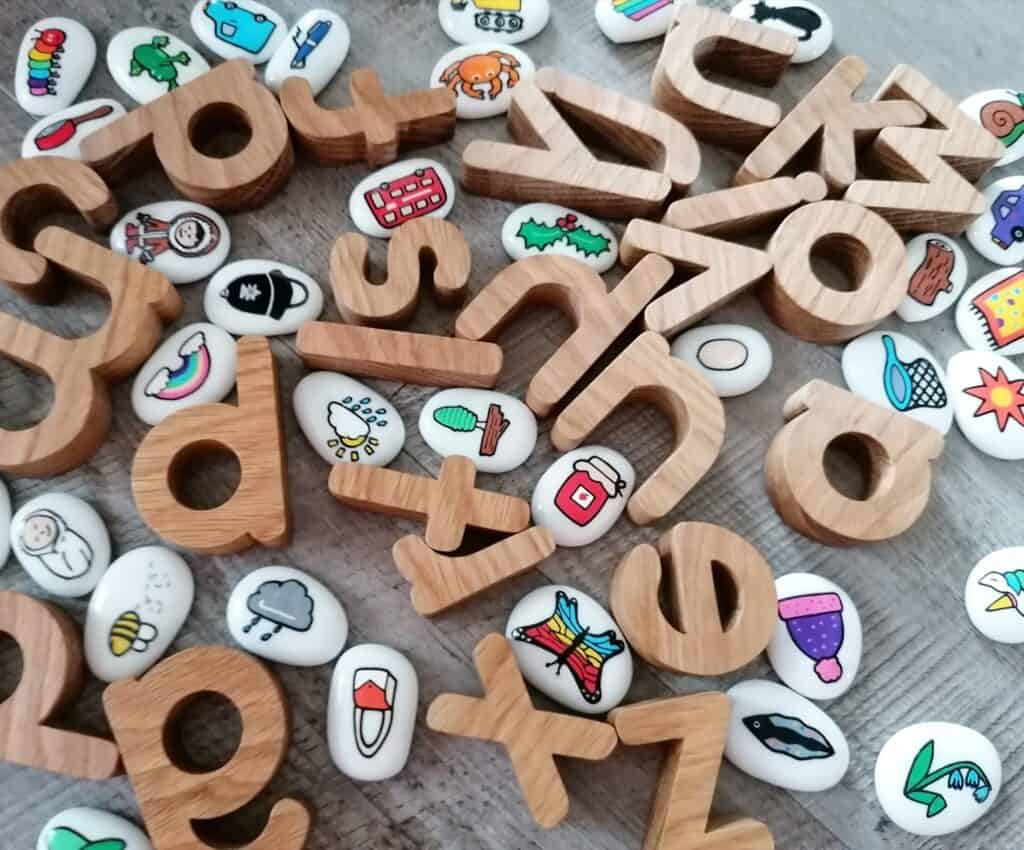 A random selection of wooden letters and white glass pebbles with different single images on.